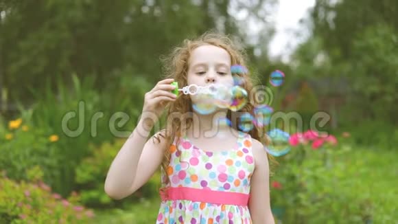 快乐的卷发女孩在夏天公园吹肥皂泡视频的预览图