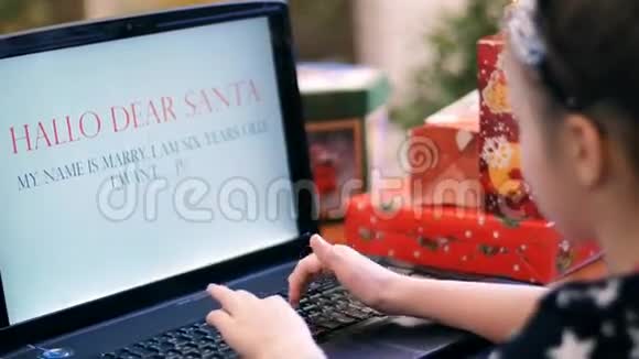 穿着漂亮裙子的可爱的金发女孩正在笔记本电脑上打印一封给圣诞老人的信信靠近一棵圣诞树上面装饰着视频的预览图