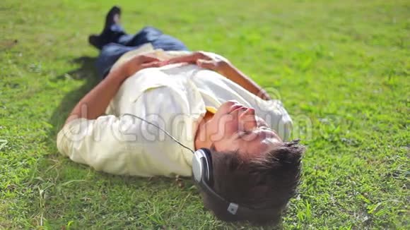 安静的黑发男人躺在草地上听音乐视频的预览图
