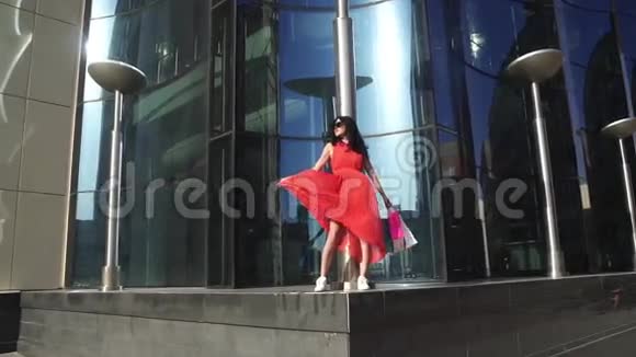 一个穿红色连衣裙长腿的年轻女孩的肖像购物后戴太阳镜的布鲁内特视频的预览图