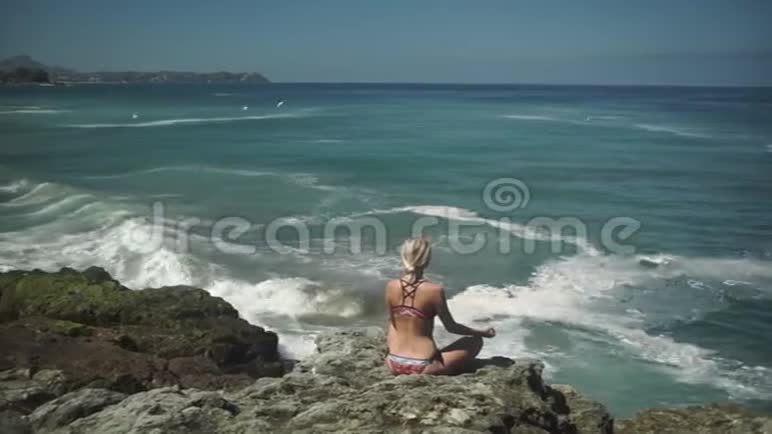 年轻女子坐在莲花的姿态在海洋附近沉思视频的预览图