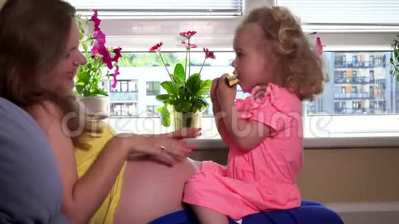 可爱的小女孩坐在怀孕的母亲膝盖上玩口风琴视频的预览图