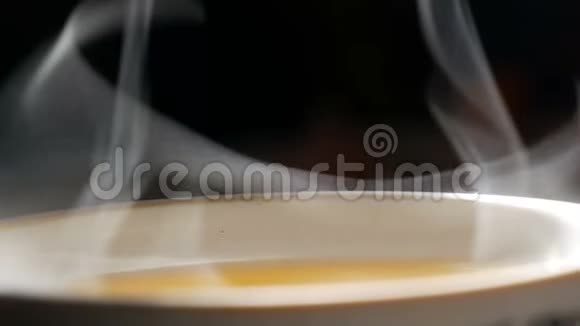 涓滴的蒸汽慢慢地从茶杯中升起近距离观看白蒸升光婀娜曲折黑色视频的预览图