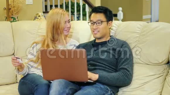 网上购物年轻的多民族夫妇通过互联网支付购买费用视频的预览图