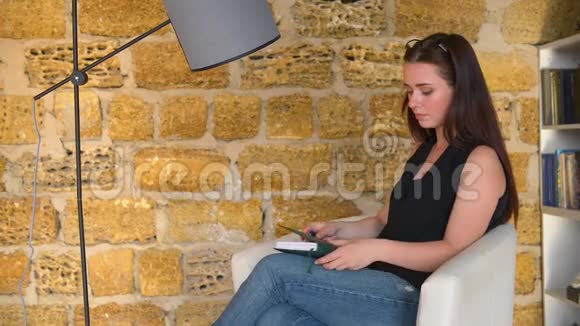 年轻的女孩女商人在一本笔记本上写下想法坐在椅子上拿着一盏灯学生正在准备视频的预览图