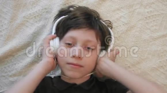 可爱的小男孩听着音乐拿着耳机看着摄像机的俯视图视频的预览图