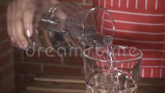 一个穿围裙的女人慢慢地把水倒进玻璃杯视频的预览图