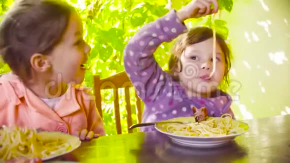 两个淘气的女孩坐在桌子旁吃意大利面和炸香肠视频的预览图