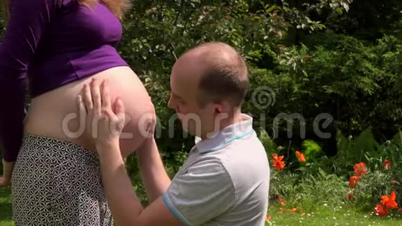 快乐的半秃老公男人在阳光下抚摸他怀孕的妻子的腹部视频的预览图