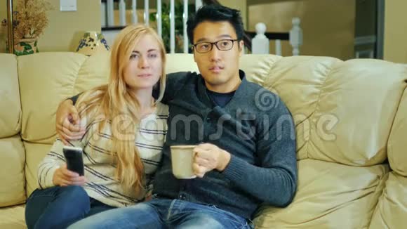 年轻夫妇一起在家看电视一个亚洲人喝咖啡或大杯茶视频的预览图