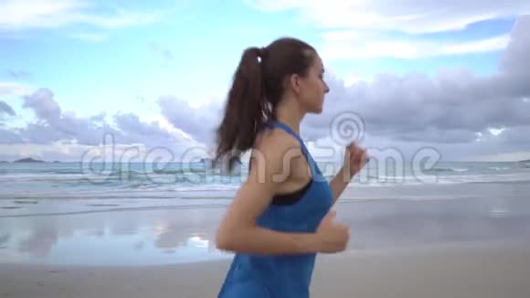 女子跑步者在海滩上与蓝天慢跑穿运动服的年轻女性视频的预览图
