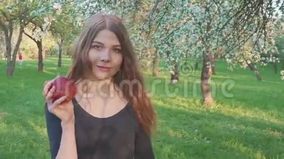 美丽的女孩手里拿着一个苹果背景是一个苹果园女人想吃苹果视频的预览图