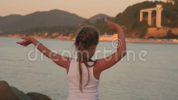 快乐的小女孩在海上张开双手享受自由夕阳海边海滩欢呼雀跃的女徒步旅行者张开双臂视频的预览图
