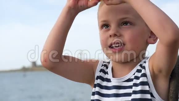 可爱的孩子穿着条纹衬衫透过望远镜在海平面前看视频的预览图