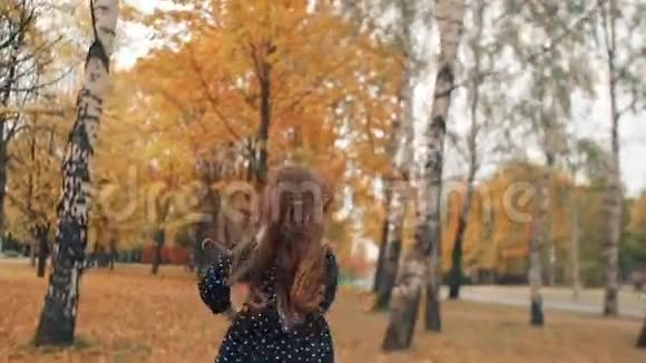 后景可爱的小女孩卷发穿着圆点裙穿过公园的秋日小巷视频的预览图