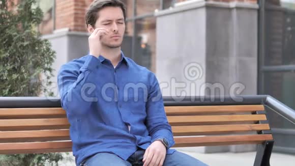 坐在户外长凳上的紧张的年轻人视频的预览图
