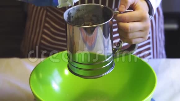 在家中的厨房里用一个绿色的碗里的筛子杯子特写一只雌性手筛面粉的慢动作烹饪视频的预览图