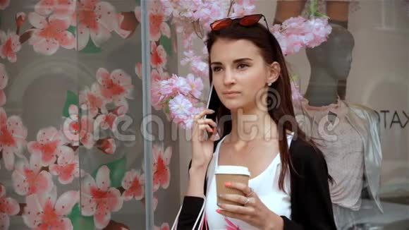 年轻女子站在商店附近喝咖啡打电话视频的预览图