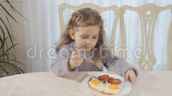 可爱的小女孩在餐桌上吃香肠和炒鸡蛋视频的预览图