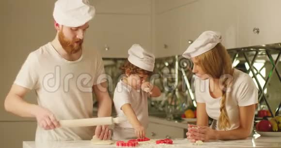 男人正在用擀面杖揉面团而他的妻子和儿子正在玩饼干模视频的预览图