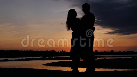 日落时分一男一女在河边的浪漫夜晚拥抱高清1920x1080慢动作视频的预览图