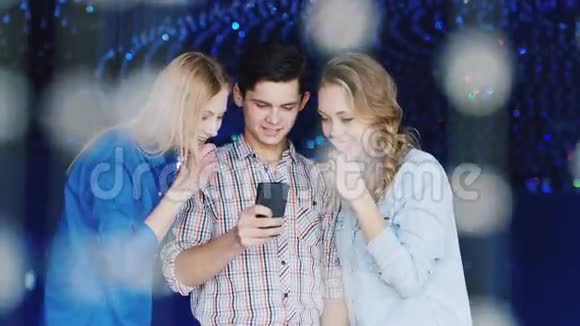 年轻的朋友男人和两个女人在夜总会使用智能手机一起看一些有趣的东西展示视频的预览图