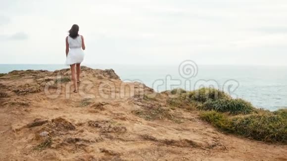 女人沿着悬崖边走日落时看着无尽的海洋视频的预览图