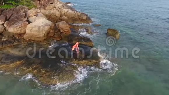 穿着亮丽泳装的女孩独自站在沙滩岩石上空中高清慢行视图泰国普吉岛视频的预览图