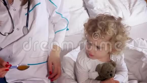 生病的孩子张开嘴和坐在床上的女医生一起吃药视频的预览图