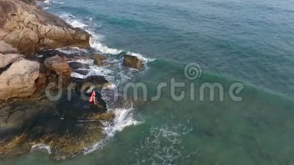 穿着亮丽泳装的女孩站在海浪拍岸空中高清慢速飞行泰国普吉岛视频的预览图