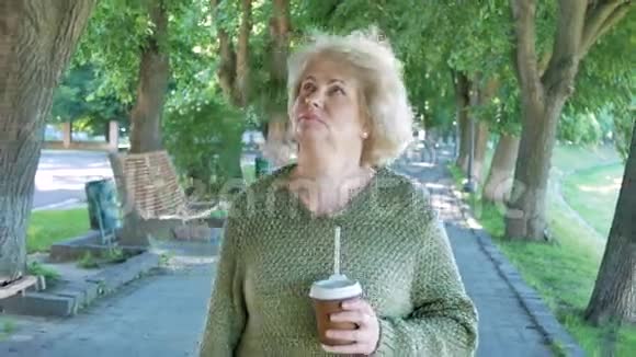 在公园小巷散步喝咖啡的老太太在公园散步的年长女性视频的预览图