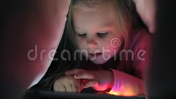 可爱的小女孩躺在毯子下拿着平板电脑视频的预览图