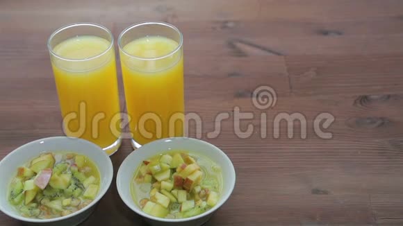 木桌上摆着两杯橙汁和两个盘子上面放着muesli和水果视频的预览图
