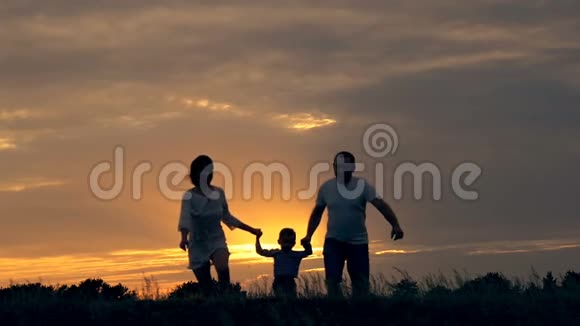 幸福的一家人在日落时在田野里奔跑夏夜一家人的剪影爱家庭的概念视频的预览图