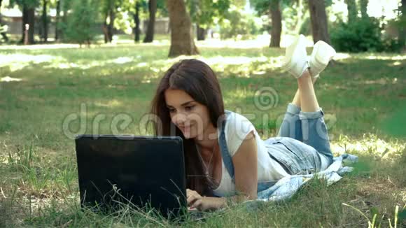 夏天躺在草地上的小女孩在笔记本电脑上打印视频的预览图