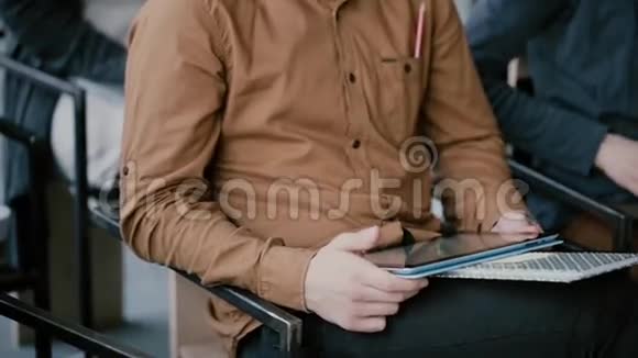 坐在椅子上的带有笔记本和数字平板电脑的年轻人的特写镜头大学研讨会或讲座的男性视频的预览图