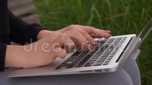在绿草附近的笔记本电脑键盘上以缓慢的动作关闭女性手臂打字视频的预览图