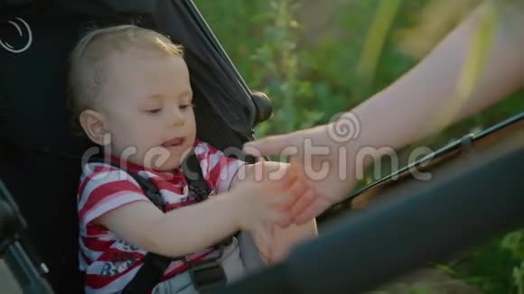 妈妈和坐在婴儿车里的小男孩玩给儿子击掌微笑着慢动作视频的预览图