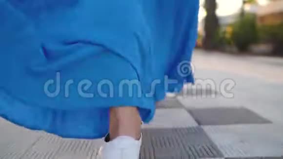 一个穿着漂亮蓝色裙子的女人在棕榈大道上行走的腿视频的预览图