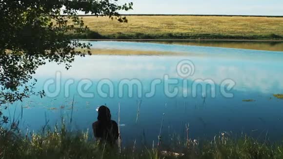 一个渔夫坐在池塘的岸边一个河流的湖钓竿被扔进水里等待着视频的预览图