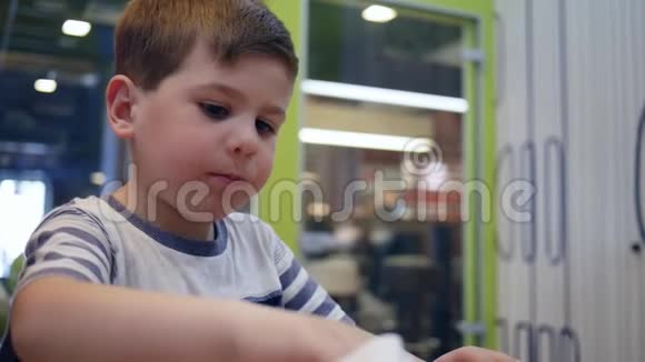 小男孩在餐桌上吃汉堡有食欲在儿童咖啡馆里给漂亮孩子吃有害食物快餐学校视频的预览图