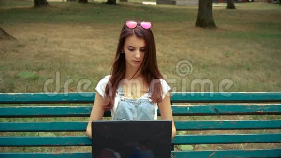 年轻可爱的女人坐在长凳上看着笔记本电脑视频的预览图