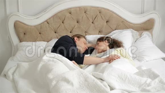 年轻的睡眠父母躺在床上可爱的小女孩在父亲和母亲身上扔枕头幸福家庭视频的预览图