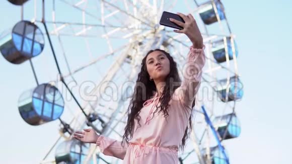 女孩站在摩天轮附近用手机自拍慢动作视频的预览图