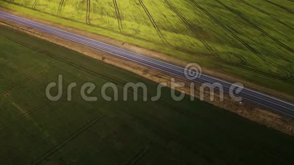 一辆汽车沿着两块田之间的乡村道路行驶的俯视图视频的预览图