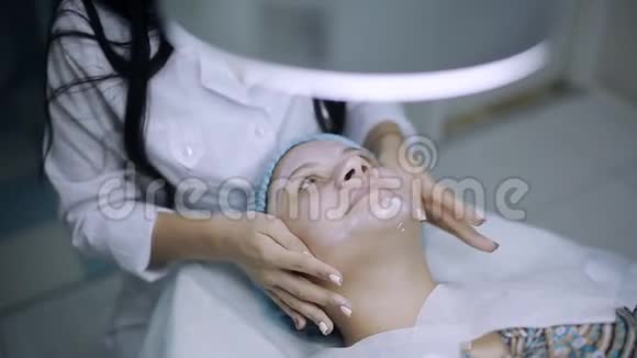 美容师在一个皮肤有问题的年轻女孩脸上涂了一个医用奶油面膜视频的预览图