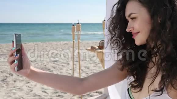 沙滩上的年轻女子手机删除节日照片微笑的女孩在背景海洋上自拍视频的预览图