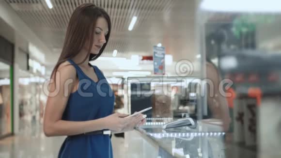 女士深色头发时尚模特购物手机NFC技术付费在超市商场机场候机楼视频的预览图