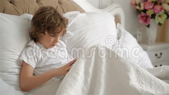 小男孩正在使用移动设备躺在床上她的妹妹正和他在一起孩子们在玩平板电脑视频的预览图