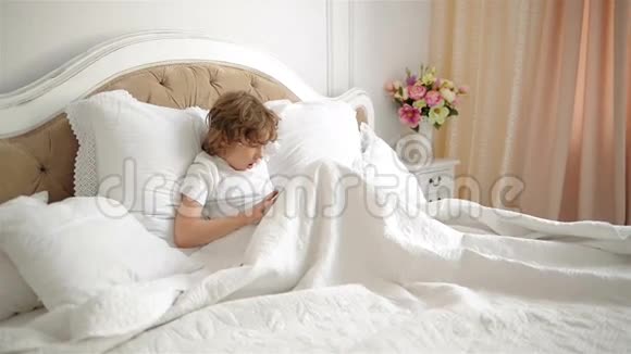 情感男孩正在用平板电脑玩电子游戏儿童床上有电子小东西的肖像视频的预览图